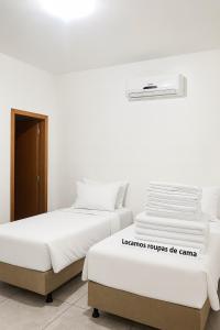two beds in a white room with a air conditioner at Casas Paradisiaca aleatória l , ll ou lll ou lV Pagamento Automática in Caldas Novas