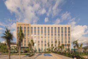 a large white building with palm trees in front of it at Hyatt Place Cancun Airport in Cancún