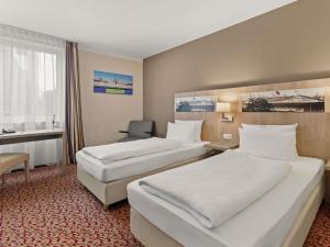 汉堡汉堡沃尔克斯公园美居酒店 的一间酒店房间，里面有两张床和一张桌子。 更多80张照片
