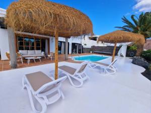 a patio with chairs and an umbrella and a swimming pool at Costa Christina con piscina climatiza in Yaiza
