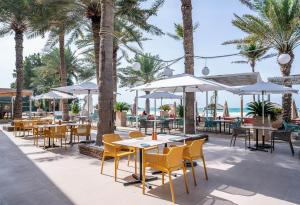 een restaurant met tafels en stoelen en palmbomen bij Occidental Sharjah Grand in Sharjah