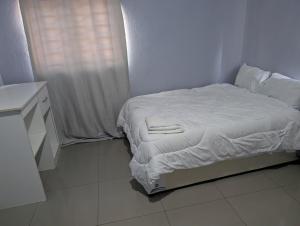 a bedroom with a bed with white sheets and a window at Gravity Apartments & Lodges in Mazabuka