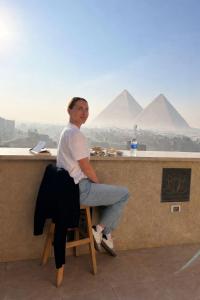 una donna seduta al bar di fronte alle piramidi di GEM Pyramids & Grand Museum View a Il Cairo