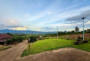 een onverharde weg naast een groen veld met uitzicht op de bergen bij Lanna Maple House in Ban Thap Dua