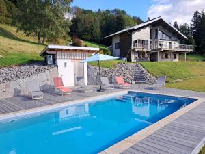 a swimming pool with chairs and a house in the background at Gîte Les Neufs Lieux in Gérardmer