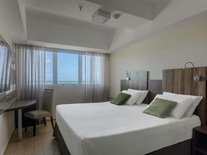 a bedroom with a large white bed with a window at Mercure Maceio Pajuçara in Maceió
