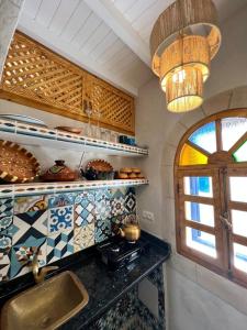 een keuken met een gootsteen, een raam en een kroonluchter bij Riad dar el hania in Essaouira
