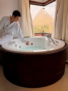 Ein Mann steht in einer Badewanne; im Hintergrund ist eine Pyramide zu sehen. in der Unterkunft New Arena pyramids VIEW in Giza + 91 Fotos