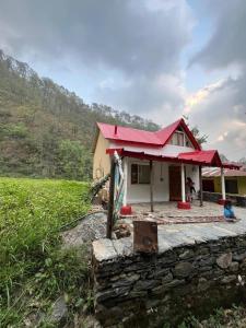 una piccola casa con un tetto rosso in un campo di Nadi Kinare a Bhimtal