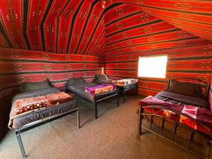 a room with three beds and a red wall at Wadi Rum Bedoun in Wadi Rum