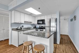 a kitchen with white cabinets and a refrigerator and two stools at Oceanfront Luxury 2BR Litchfield Beach Escape in Pawleys Island