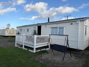 a white mobile home with a porch and a swing at Coastal Beachfront Caravan in Brightlingsea