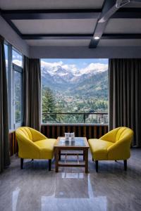 a living room with yellow chairs and a table and a large window at Apple Flower Mountain View Hotel in Manāli