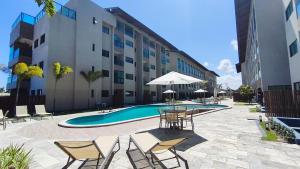 een zwembad met stoelen en tafels en een gebouw bij Max Carneiros Suítes - Com e sem piscina privativa in Praia dos Carneiros