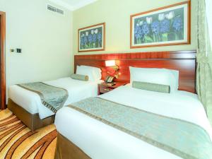 a hotel room with two beds and two pictures on the wall at Grand Mercure Majlis Residences Abu Dhabi in Abu Dhabi