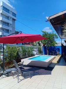 American Hostel e Pousada في جوينفيل: مسبح فيه مظله حمراء وكراسي ومسبح