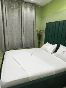 - une chambre avec un grand lit blanc et une tête de lit verte dans l'établissement HOTEL COMFORT INN & SUITEs, à Yaoundé