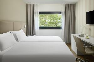 2 Betten in einem Hotelzimmer mit einem Schreibtisch und einem Fenster in der Unterkunft NH Madrid Ventas in Madrid