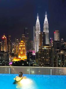 a man in a pool with a city skyline at night at The Luxe KLCC by Infinitum in Kuala Lumpur