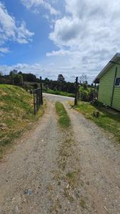 a dirt road next to a green building and a fence at Cabañas El Maiten de Castro in La Chacra