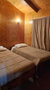 two beds in a room with wooden walls at Cabañas El Maiten de Castro in La Chacra