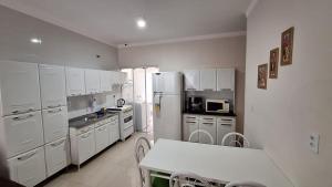 a kitchen with white cabinets and a table and a refrigerator at Casa Requinte in Cascavel
