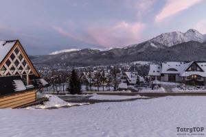 een groep gebouwen in de sneeuw met bergen bij TatryTop Giewont House in Kościelisko