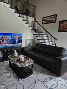 ein Wohnzimmer mit einer schwarzen Couch und einem Fernseher in der Unterkunft Downtown Access • Fenced Yard • Sleeps 10 in McKinney