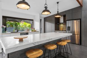 a kitchen with a white counter and wooden stools at Summit to Sea, Elevated Luxury in Coolum Beach