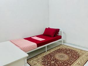 a small bed with a red pillow and a rug at Homestay Hayyan in Kampong Terbak