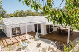 a white house with a deck and chairs at Ocean Haze - Putting Green, Firepit, Beach location in Mollymook