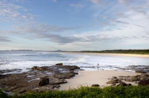 a beach with rocks and the ocean with waves at The Marlin House Iluka in Iluka