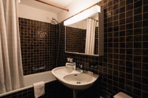 un bagno piastrellato nero con lavandino e specchio di Casa Partnun 4-3 a Laax-Murschetg