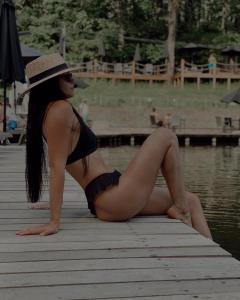 een vrouw in bikini en hoed zit op een steiger bij Характер парк in Hatne