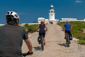 trois personnes à vélo sur un chemin de terre avec un phare dans l'établissement Chalet Addaya, à Port d'Addaia