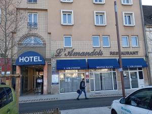 Ein Mann geht eine Straße vor einem Hotel entlang in der Unterkunft Hotel Restaurant l'Amandois in Saint-Amand-Montrond