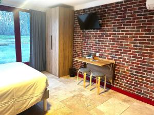 a bedroom with a bed and a desk with a tv on a brick wall at Logis Hôtel Les 200 Bornes in Pouilly-sur-Loire