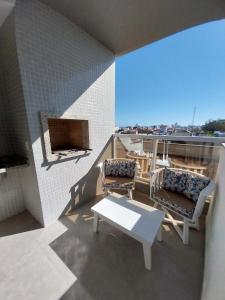 ein Balkon mit zwei Stühlen und einem Tisch auf einem Gebäude in der Unterkunft Modern apartment steps from the beach with amenities in Arroio do Silva