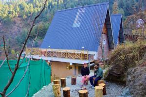 two people sitting on benches outside of a building at The Clifton chapter tirthan in Gushaini