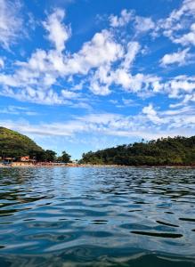 une grande étendue d'eau avec des arbres et un ciel bleu dans l'établissement Casa Lopes temporada Ubatuba, à Ubatuba
