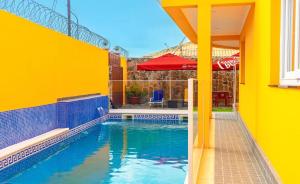 a yellow house with a swimming pool with a red umbrella at Saton 24H Guest House in São Tomé