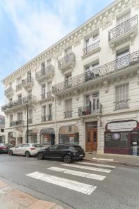 ein großes weißes Gebäude, vor dem Autos parkten in der Unterkunft Le Cedre - Appartement cosy dans le centre de Vichy in Vichy