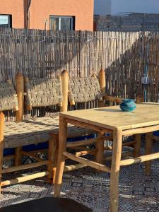 a wooden table and benches in front of a fence at Blue Pearl Surf & Yoga House in Tamraght Ou Fella