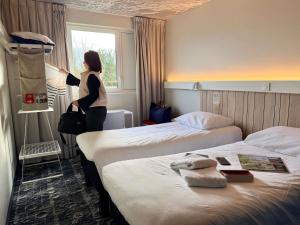 una donna in piedi in una stanza d'albergo con due letti di ibis Rennes Cesson a Cesson-Sévigné