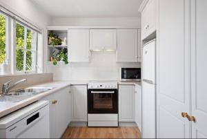 een witte keuken met witte kasten en een zwarte oven bij Kowhai Apartment-Ground Floor in Pukekohe East