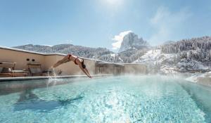 a person jumping into a swimming pool in the mountains at Hotel Touring Dolomites in Santa Cristina Gherdëina