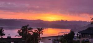 een zonsondergang boven een waterlichaam met palmbomen bij Country Harbourside Escape in Whakapirau +7 foto's