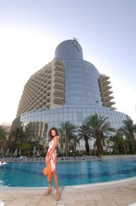 a woman standing in front of a swimming pool at Royal Dead Sea - Hotel & Spa in Ein Bokek