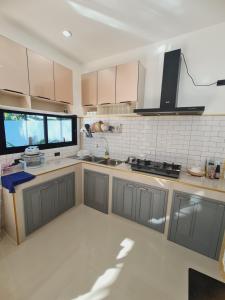 een keuken met grijze kasten en een groot raam bij สกลนครพูลวิลล่า in Sakon Nakhon