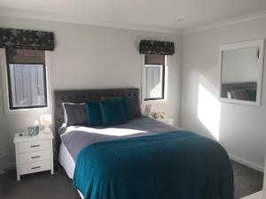 a bedroom with a bed with a blue blanket and two windows at Parklands paradise 3bedroom4beds in Napier